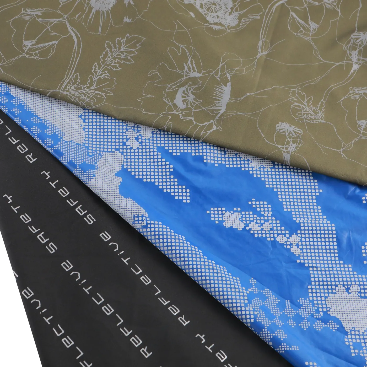 Printed reflective fabric — olive floral print, blue halftone print and black lettering print stacked